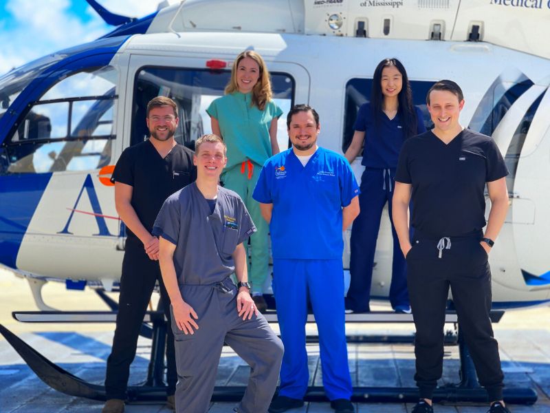 Six pediatric emergency fellows stand together in front of a helicopter.